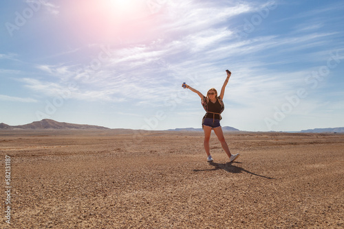 The model joyfully raised her hands to the mountain on the background of the desert. Sunny day on vacation. Behind is a model of hilly mountains. The model is happy about the trip and the day off. 