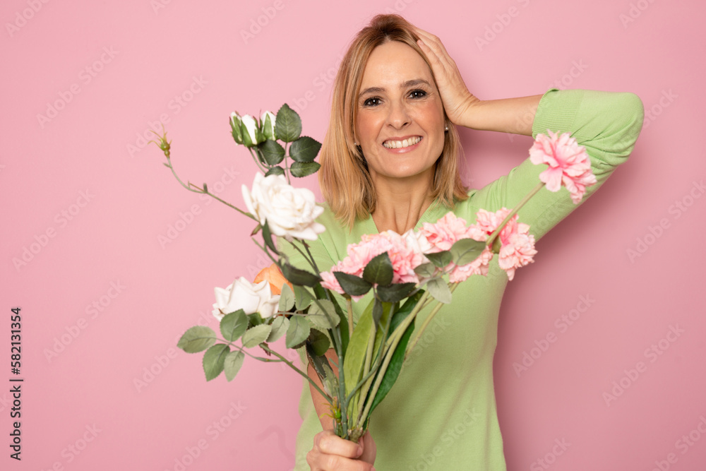 Portrait of a beautiful young woman in dress holding big bouquet of flowers isolated over pink background