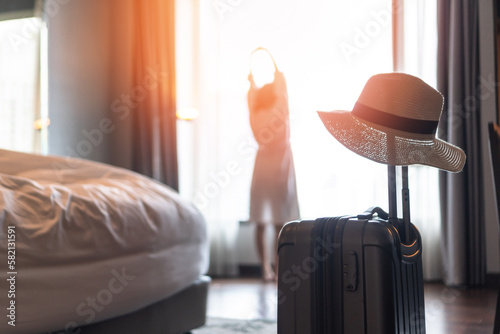 Traveller woman with luggage in business hotel guest room looking out toward city view staying for work travel or vacation trip