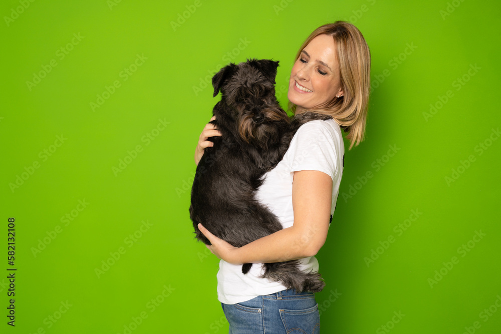 Portrait of attractive cheerful careful girl holding in hands doggy schnauzer isolated over bright green color background