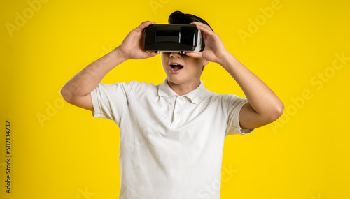 Portrait of young asianman play ing virtual reality on yellow background