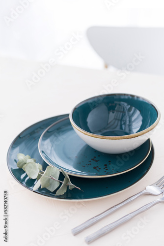 Fototapeta Naklejka Na Ścianę i Meble -  Three empty green plates with silver cutlery on white table in front of window. Set of three various plates on table. Minimal style table setting