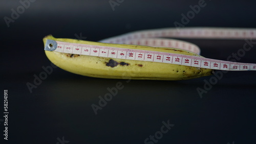 Yellow Banana with Measuring Tape Isolated on Black Background. comparable to man penis size as short, small medium, average, long,large size and extra large size