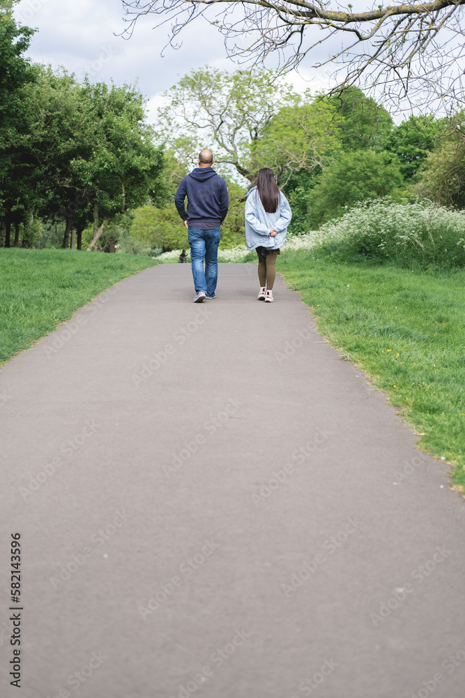 Vertical photo of a multicultural couple walking on a footpath in Figgate Park in Edinburgh in spring time. Biracial family.