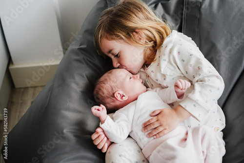 happy big sister toddler kissing newborn baby girl at home during daytime.Family and childhood