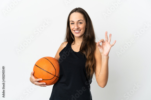 Young hispanic woman over isolated white background playing basketball and making OK sign