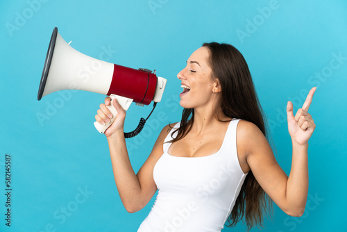 Young hispanic woman over isolated blue background shouting through a megaphone to announce something in lateral position