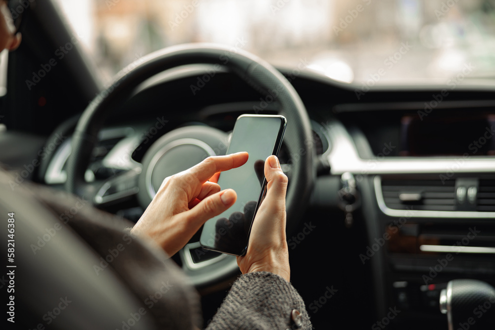 Close up of female driver hands is using phone while sitting behind steering wheel in own car Close up of female driver hands is using phone while sitting behind steering wheel in own car