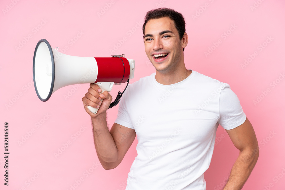 Young caucasian man isolated on pink background holding a megaphone and smiling Young caucasian man isolated on pink background holding a megaphone and smiling
