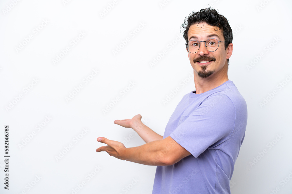 Young man with moustache isolated on white background extending hands to the side for inviting to come Young man with moustache isolated on white background extending hands to the side for inviting to come