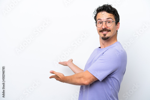 Young man with moustache isolated on white background extending hands to the side for inviting to come