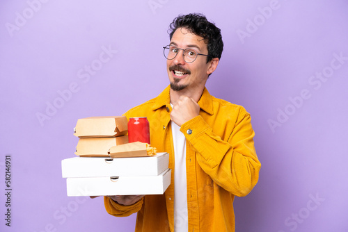 Young caucasian man holding fast food isolated on purple background celebrating a victory