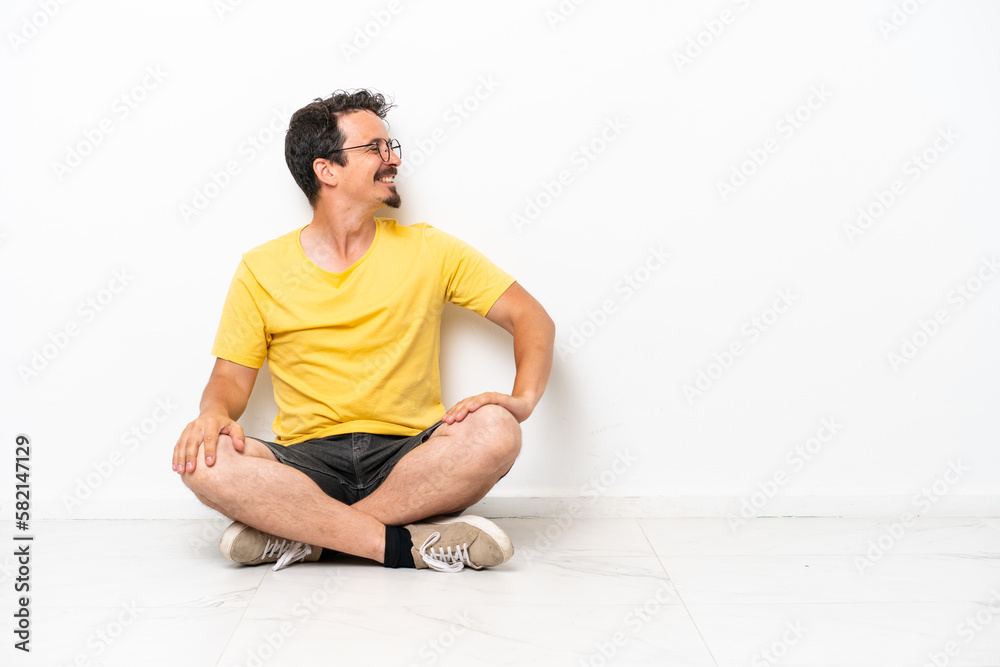 Young caucasian man sitting on the floor isolated on white background in lateral position Young caucasian man sitting on the floor isolated on white background in lateral position