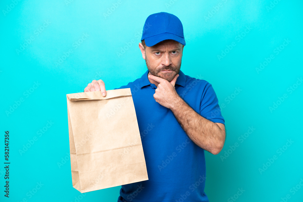 Middle age man taking a bag of takeaway food isolated on blue background thinking Middle age man taking a bag of takeaway food isolated on blue background thinking