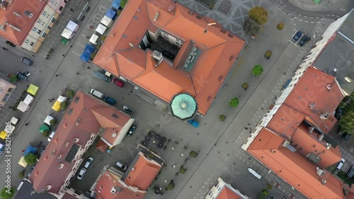 Top-down drone footage showing historical market square of the city, containing building with green tower above which drone hovers and rotates. Visible pedestrains and strollers.  photo