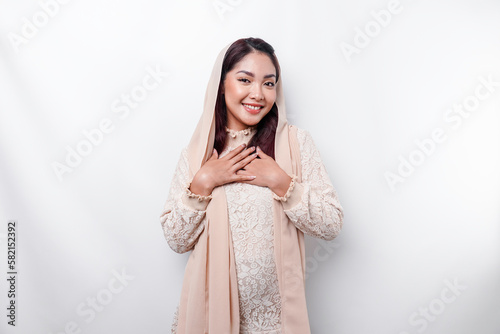 Happy mindful thankful young Asian Muslim woman with her hand on her chest smiling isolated on white background