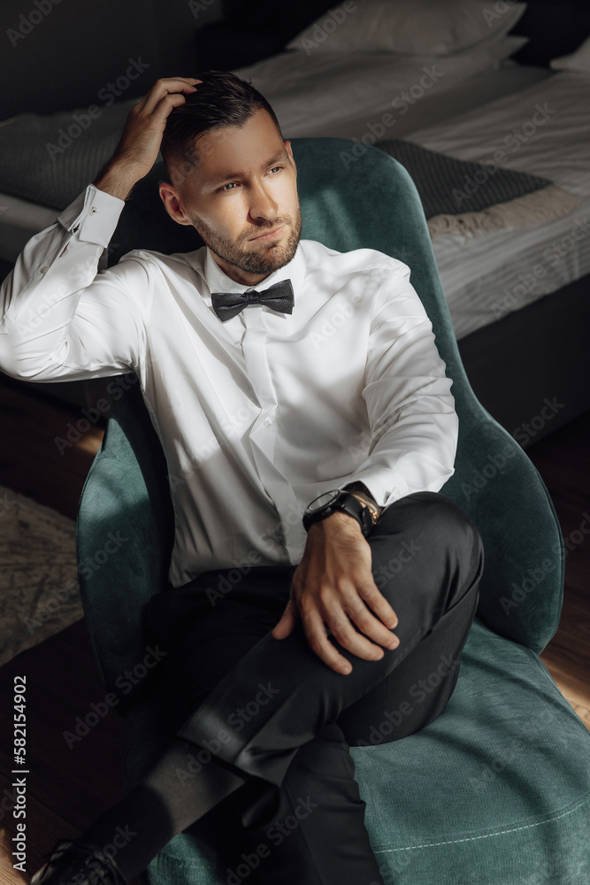 The stylish bridegroom poses for the photo, prepares for the wedding ceremony. Large portrait. Wonderful interior in the morning light. The groom's morning The stylish bridegroom poses for the photo, prepares for the wedding ceremony. Large portrait. Wonderful interior in the morning light. The groom's morning
