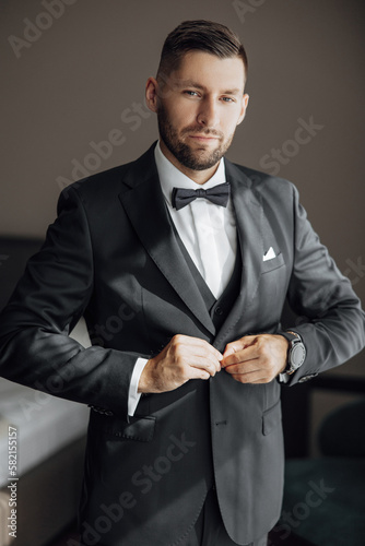 Stylish groom portrait getting ready in the morning for wedding ceremony. Morning of the groom. Groom morning preparation. The groom puts a black jacket. A large portrait