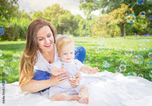Healthy child (kid) having fun with mother and soap bubbles in a sunny summer day at the park. Caucasians happy baby (boy). Healthy lifestyle, family, childhood, Mother's Day.