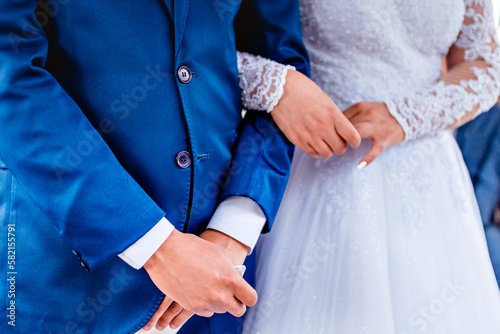 the hand of a groom in a blue suit intertwined with the hand of a bride dressed in white