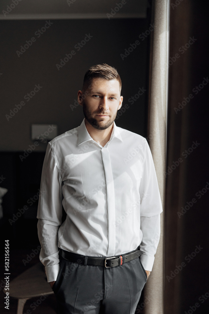 The stylish bridegroom dresses, prepares for the wedding ceremony. Large portrait. Wonderful interior in the morning light. The groom's morning