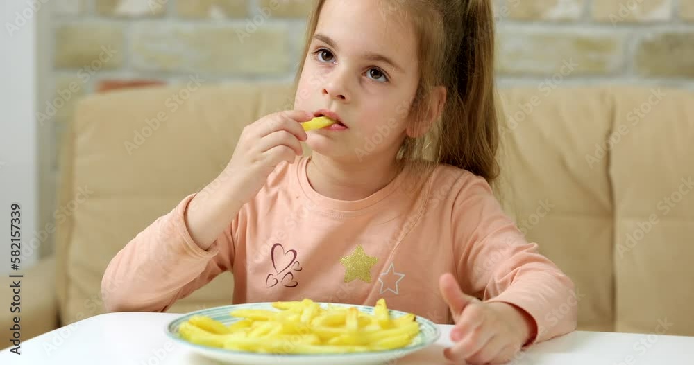 Little hungry girl eating french fries at home and watching tv Little hungry girl eating french fries at home and watching tv