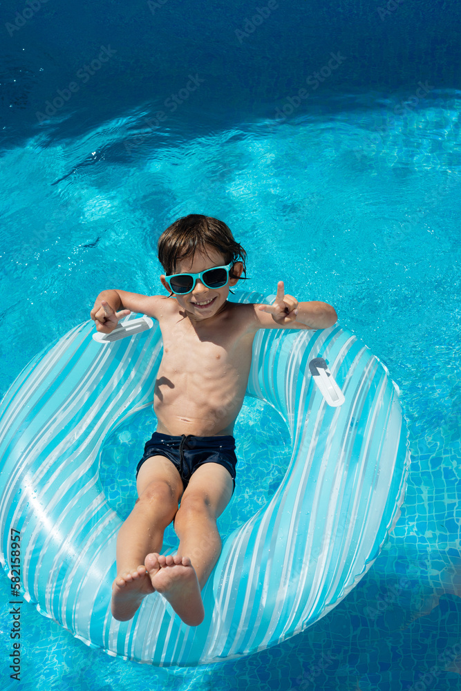 Boy on inflatable swim ring and sunglasses in swimming pool