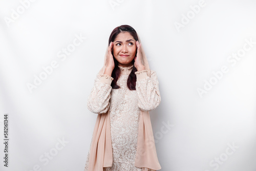 A thoughtful young Asian Muslim woman wearing headscarf while looking aside, isolated by a white background