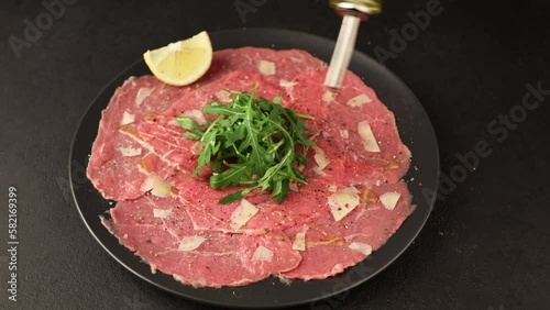 Marbled beef carpaccio with arugula, parmesan cheese, olive oil and lemon. A traditional classic appetizer made from thinly sliced raw meat. Pour olive oil. Close-up, selective focus, black background