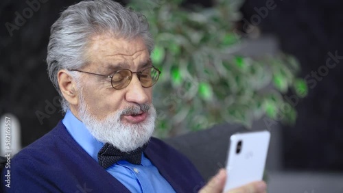 A close-up of an elderly man holding a phone communicates via video chat with relatives, friends, family learned unpleasant news