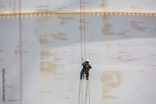 Male worker down height tank roof rope access safety inspection thickness weld of storage tank.