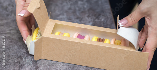 five macaroons in paper packaging on the table. unpacking process. hands close up. home bakery concept.