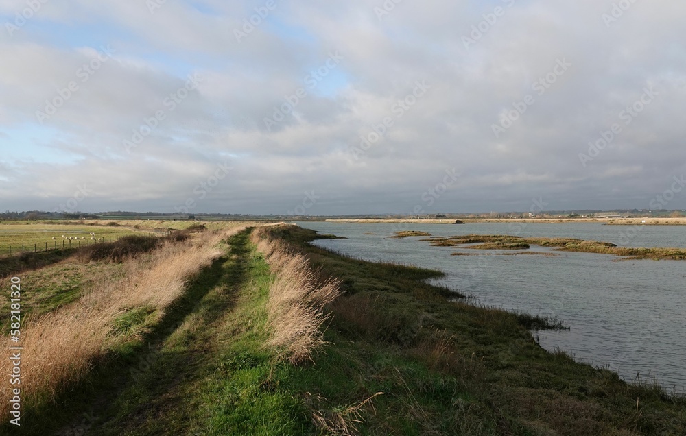 Footpath by the river under a cloudy sky at Old Hall Marshes, Essex, UK