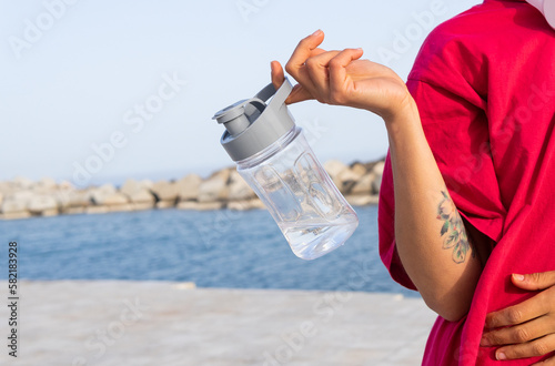 Crop woman with bottle of water on embankment