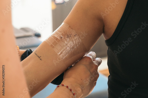 Unrecognizable woman master covering tattoo with plastic tape photo