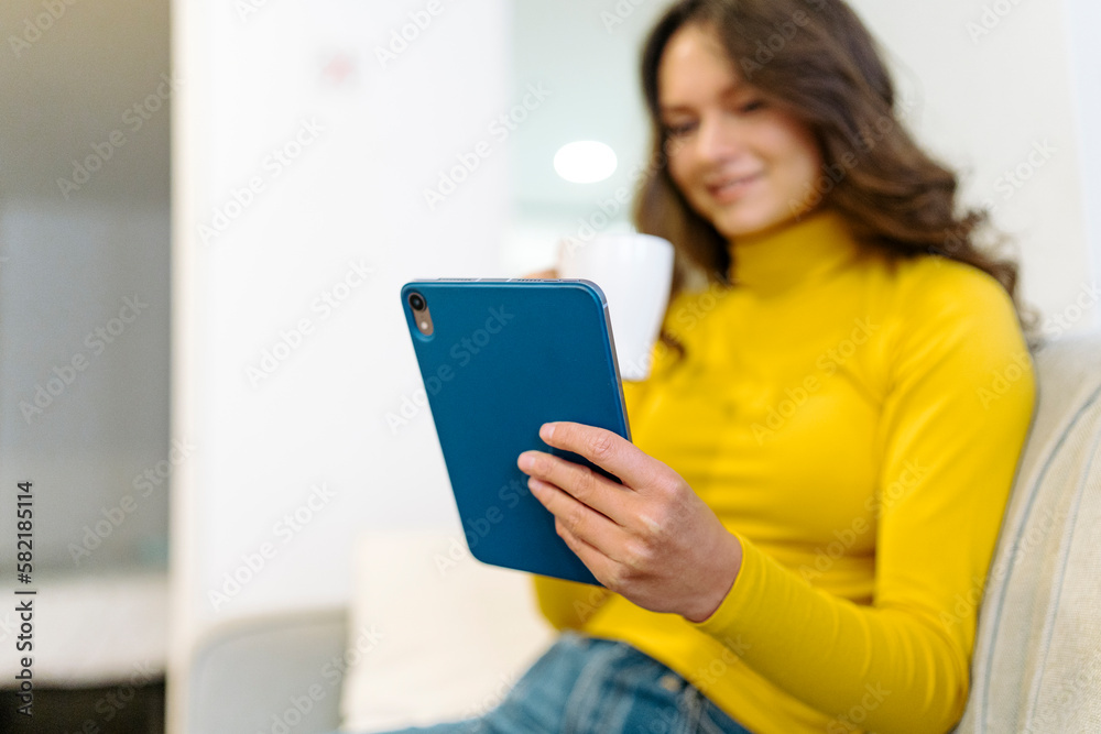 Focused happy woman with coffee browsing tablet on sofa Focused happy woman with coffee browsing tablet on sofa