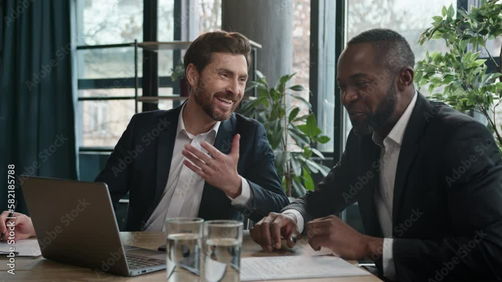 Two happy satisfied multiracial men diverse businessmen in office meeting talking laughing with laptop document partnership working with project Caucasian man executive manager African American worker