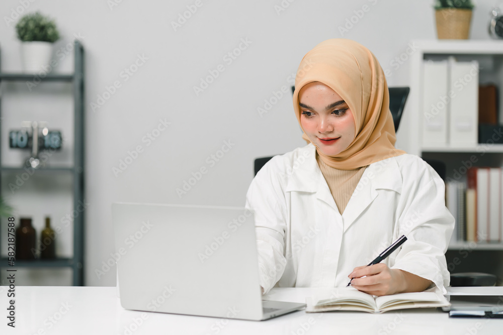 Beautiful muslim business woman wearing a hijab is diligently working at her computer, displaying professionalism and commitment to her job.
