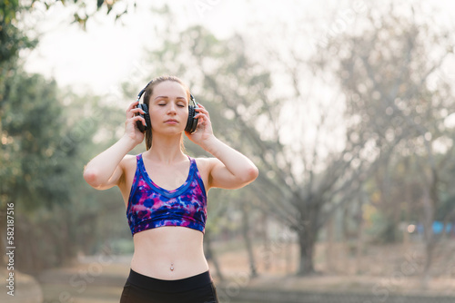 A relaxed woman is shown enjoying music while jogging through a public park. The young lady is feeling free, relaxed, and happy.