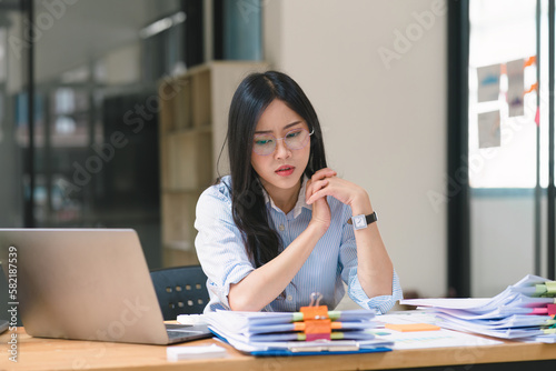 The tired businesswoman is feeling sleepy and bored from sitting at her desk for a long time, and may be experiencing symptoms of office syndrome. © kenchiro168