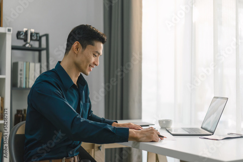 A young businessman is shown working on a laptop computer in his home office. The image represents the concept of working from home.