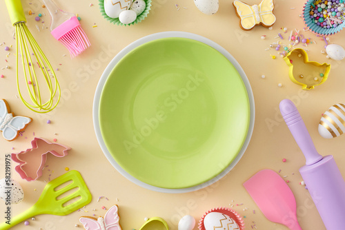Easter cooking idea. Flat lay composition of empty green plate white golden easter eggs cookies kitchen utensils baking molds and sprinkles on isolated beige background