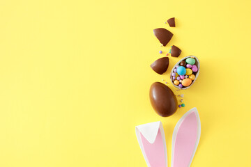 Easter sweets idea. Top view photo of rabbit bunny ears chocolate egg сolorful candies and chocolate pieces on isolated yellow background with empty space