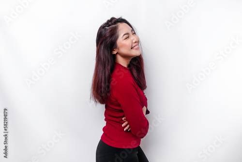 Portrait of a confident smiling Asian woman dressed in red, standing with arms folded and looking at the camera isolated over white background © Reezky