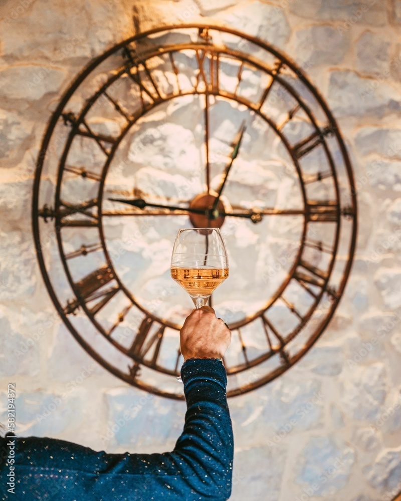 Vertical shot of a hand holding a glass of rose wine before the clock