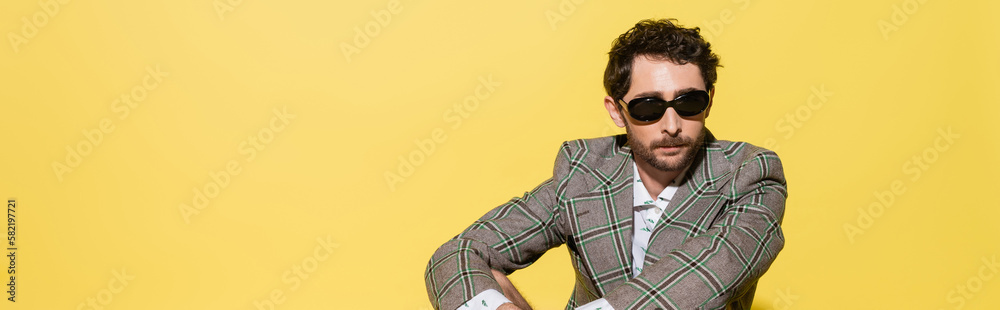 Charming guy in checkered jacket and sunglasses isolated on yellow, banner.