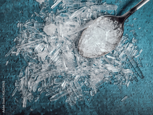 A metal spoon filled with natural menthol crystals on blue background.