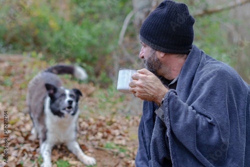 man drinking a cup of coffee with his dog in the background © Jose Antona/Wirestock Creators