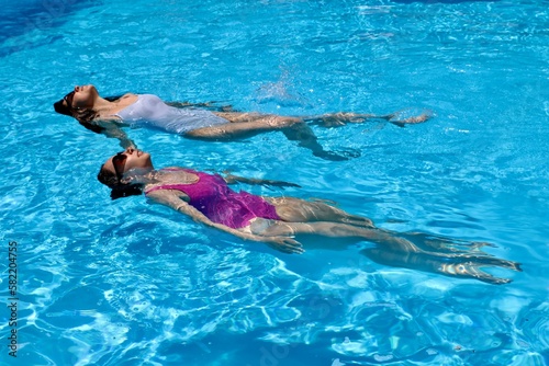 Attractive women in swimsuits swimming on their backs in the pool