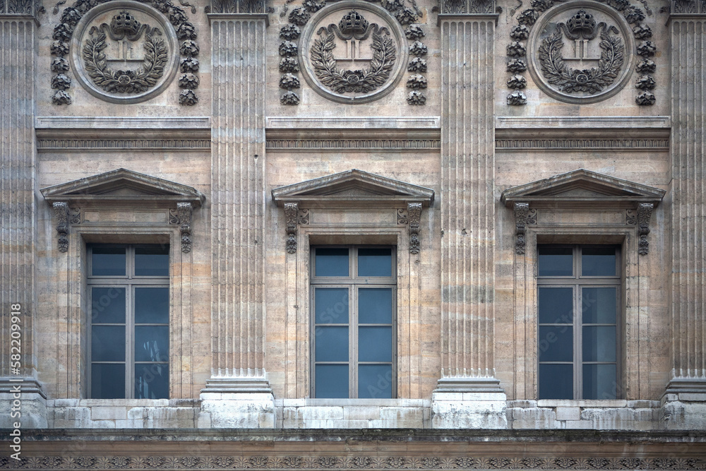 Paris ancient stone building facade with three French windows and rich stucco fretwork.